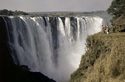 Tourists look small against backdrop of Victoria Falls, Zimbabwe. Named by the British explorer David Livingstone in honor of Queen Victoria, the falls are also known as Mosi oa-Tunya.